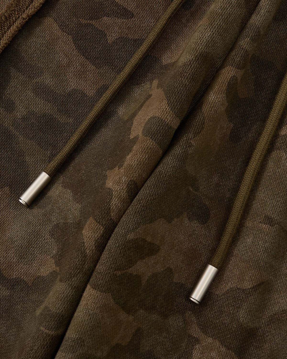 Close-up of Sundae School’s CAMO MOCHI HAZE PANELED SWEATPANTS, crafted from 100% cotton camouflage fabric with two olive green drawstrings tipped in silver metal, featuring a soft, slightly fuzzy texture.