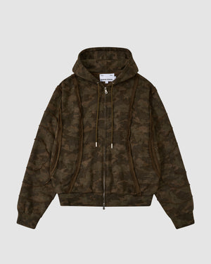 The Sundae School CAMO MOCHI HAZE PANELED ZIP UP HOODIE is a brown and green camo 100% cotton jacket with zipper front, drawstrings, ribbed cuffs, and an inside collar label, shown on a light gray background.