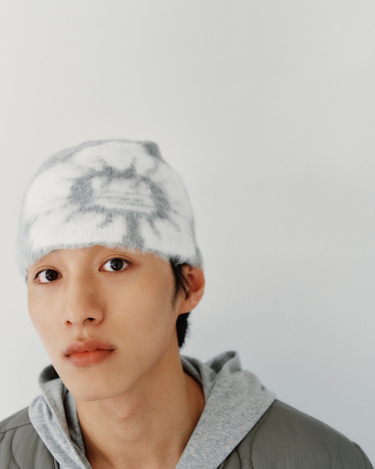 A person wearing a grey and white tie-dye GREY DDUL BEANIE as protective headgear and a grey hoodie.