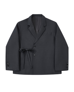Introducing the CHARCOAL DOUBLE DUTY BLAZER by Sundae School—a refined wool blend blazer in deep charcoal, featuring notched lapels, front button closure, a chest pocket, and a fabric belt elegantly tied at the waist. Inspired by the silhouette of a hanbok, this design is finished with subtle button accents near the cuffs for an elevated touch.