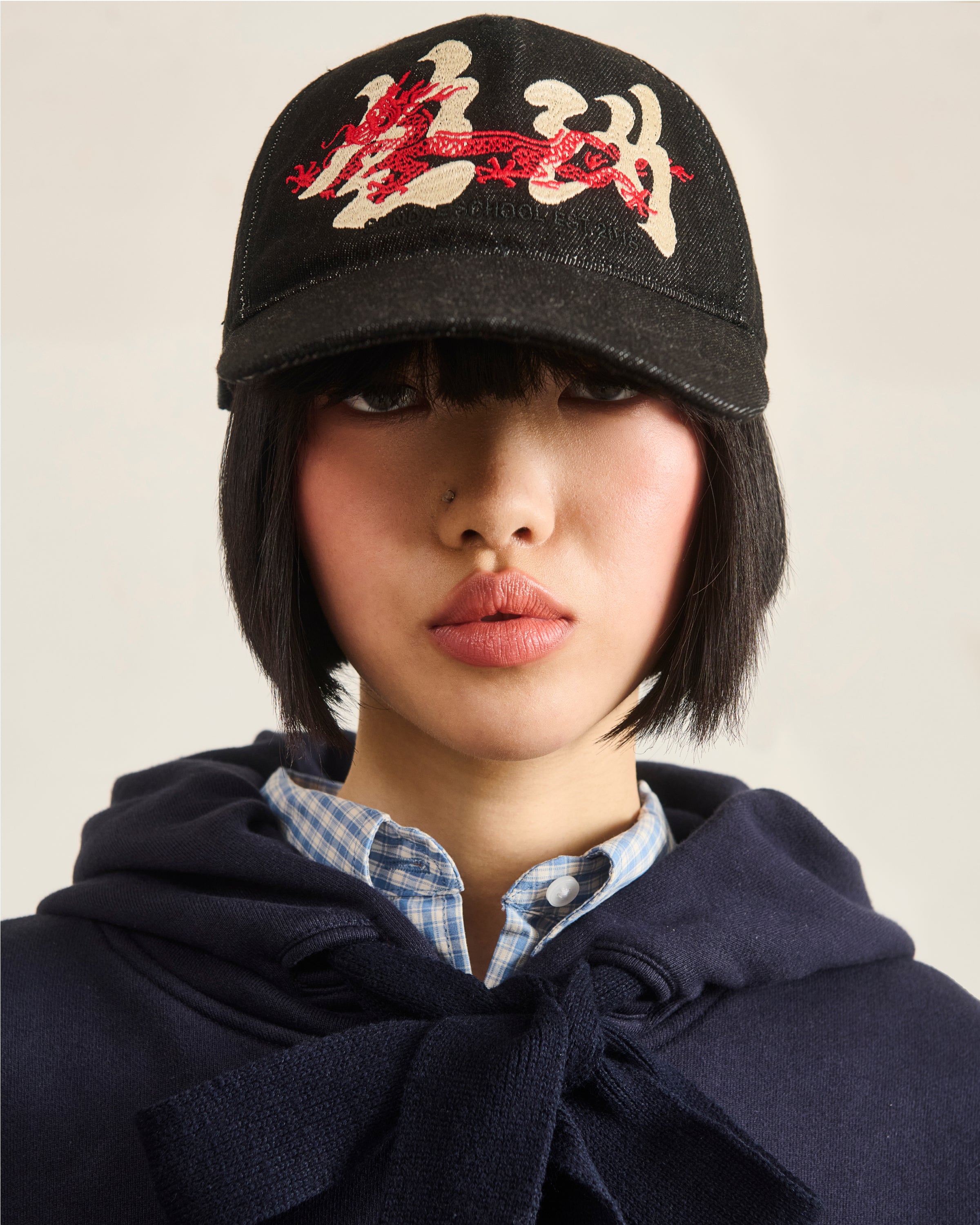 Person wearing a black cap with red and white designs on a neutral background