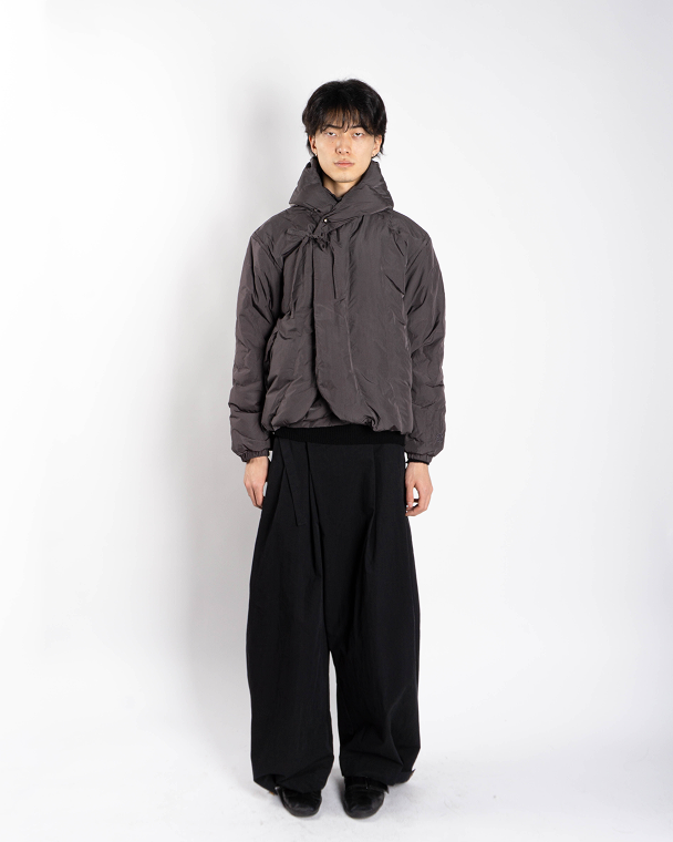 The CHARCOAL HEAVYWEIGHT MOCHI PUFFER by Sundae School, a dark brown winter jacket with a high collar, diagonal button closure, and elastic cuffs, is laid flat on a plain light gray background.