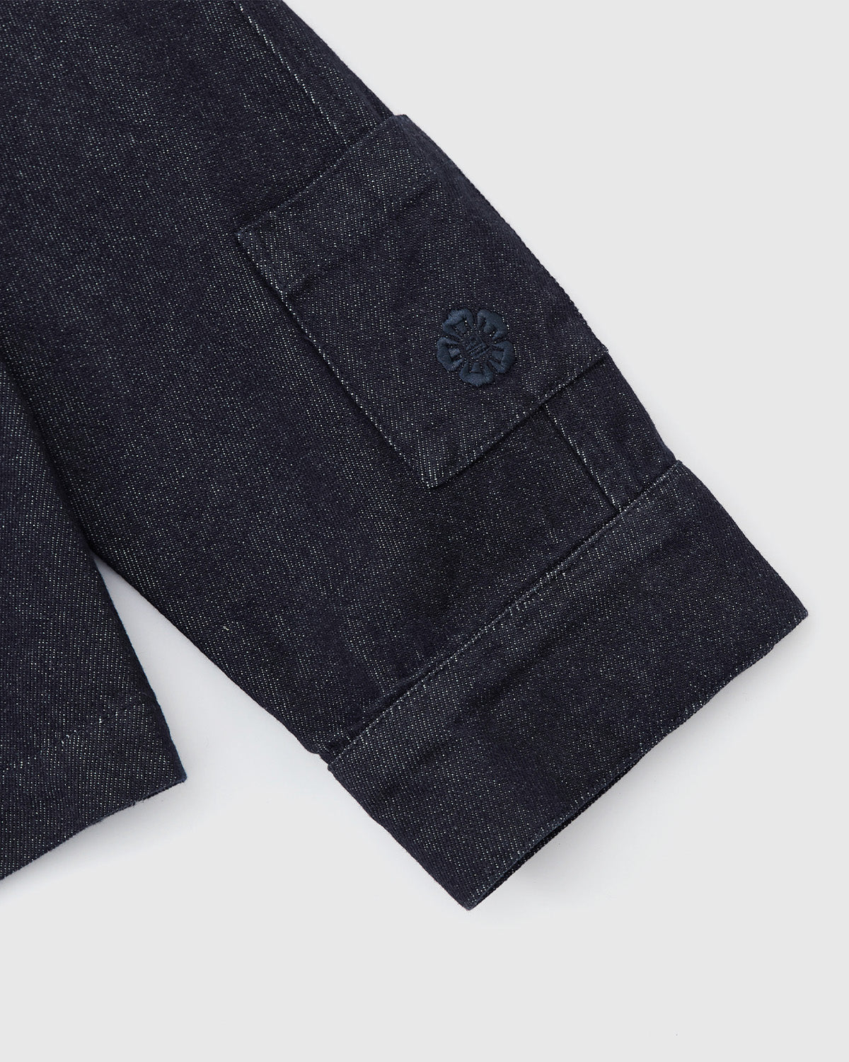 Close-up of the Sundae School DENIM CHORE JACKET sleeve, showing a folded cuff and a small pocket with an embroidered flower on the flap.