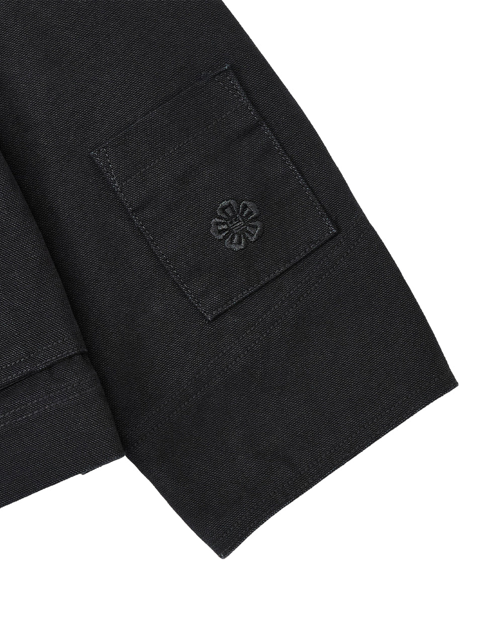 Close-up of the BLACK FIREMAN CLASP JACKET by Sundae School, showcasing a black fabric sleeve with a small patch pocket accented by a delicate embroidered flower motif reminiscent of custom Mochi Floral clasps. The visible texture of the fabric lends a refined vintage touch to the piece.