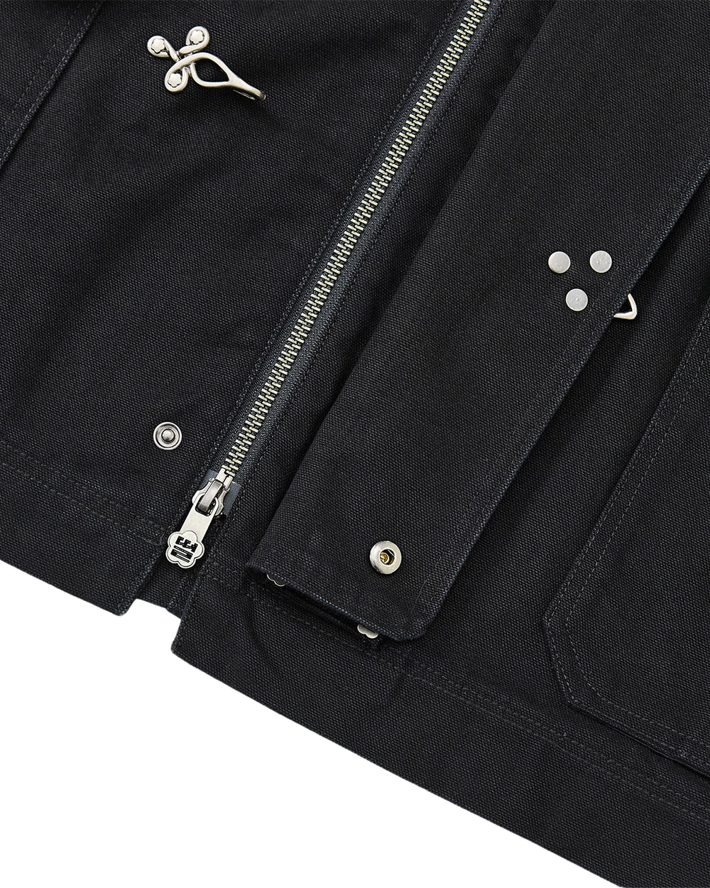 Close-up of the BLACK FIREMAN CLASP JACKET by Sundae School, showcasing its silver zipper, metallic snap buttons, and signature Mochi Floral clasps alongside decorative metal pins. The image highlights the detailed stitching, textured fabric, and subtle vintage-inspired finish.