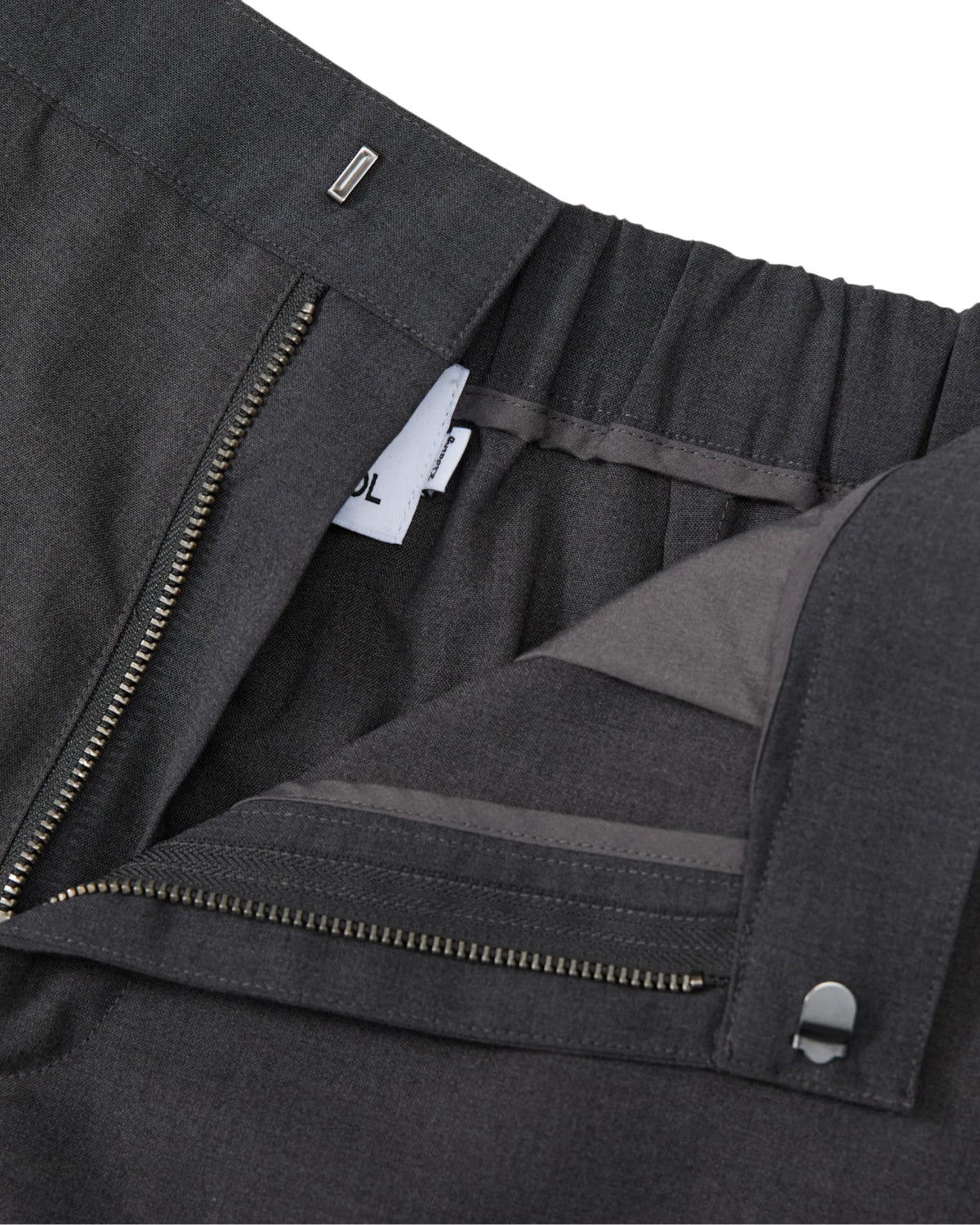 Close-up of Sundae School FLARE SKIRT PANTS in dark gray, featuring a semi-bootcut silhouette, an open zipper, a visible waistband with elastic at the back, and a small white clothing tag inside.