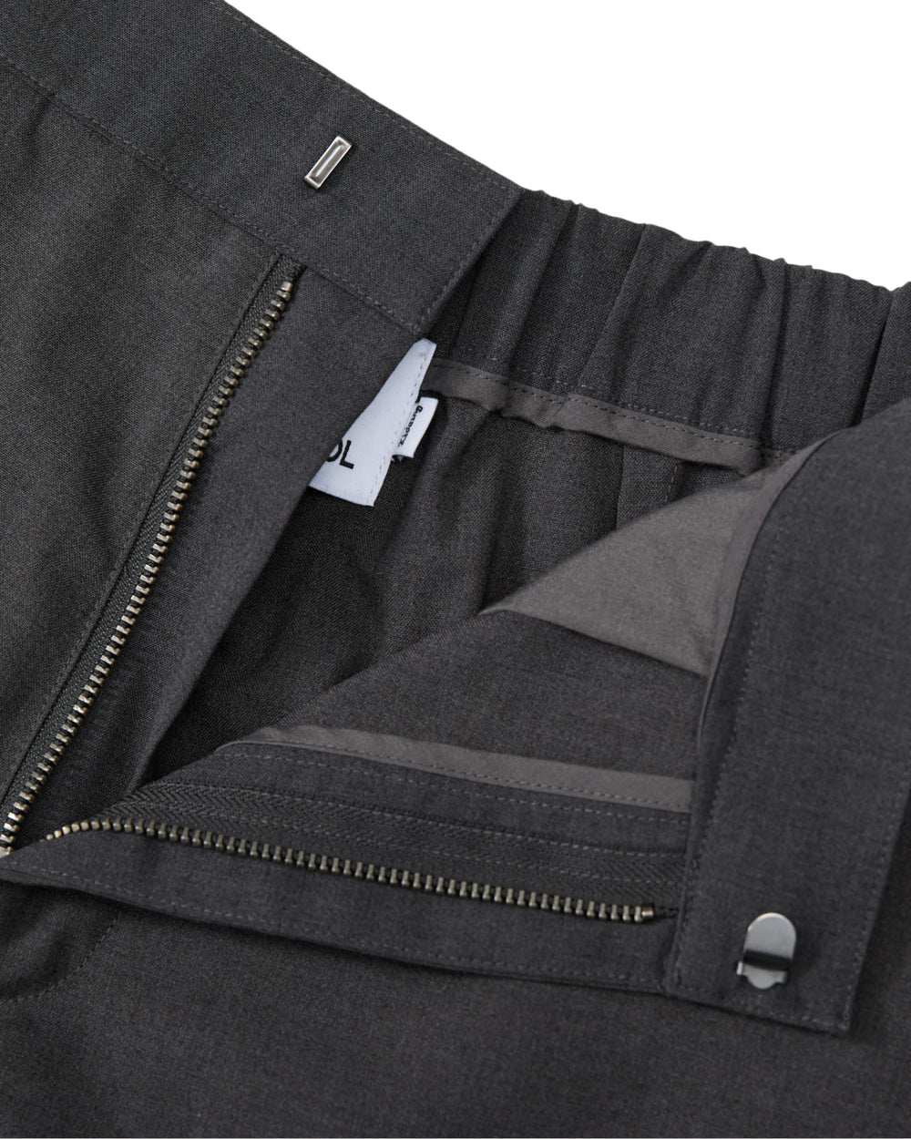 Close-up of Sundae School FLARE SKIRT PANTS in dark gray, featuring a semi-bootcut silhouette, an open zipper, a visible waistband with elastic at the back, and a small white clothing tag inside.