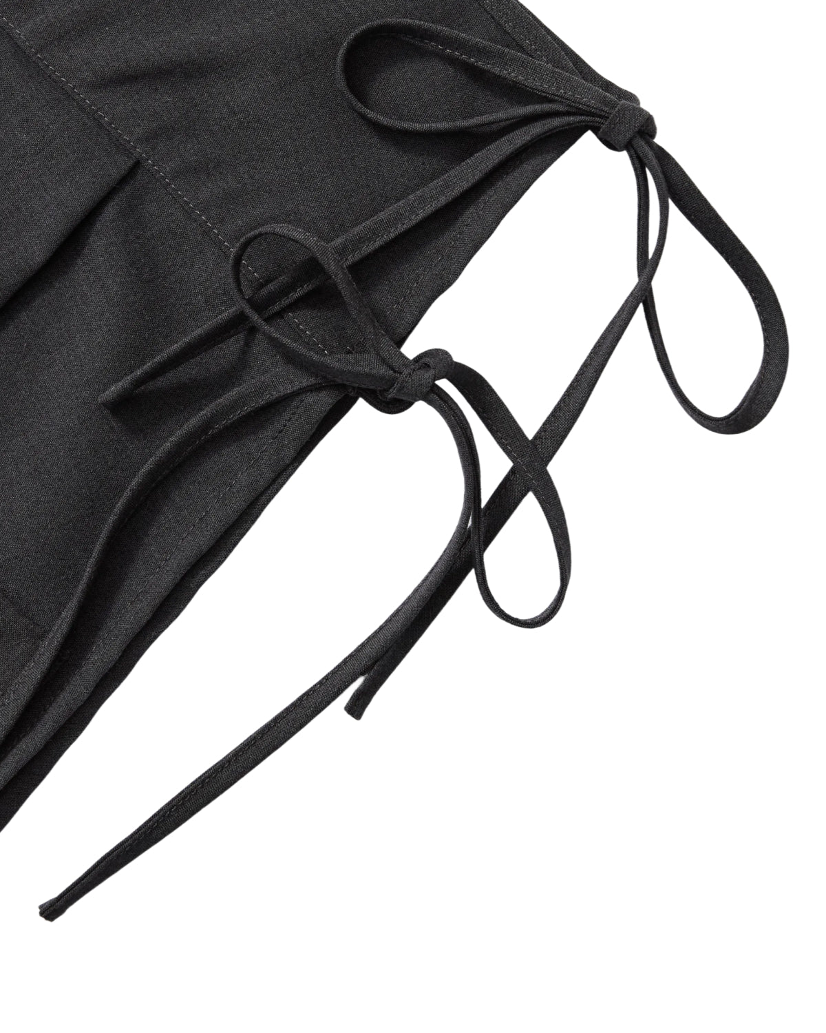 Close-up of two fabric straps tied into neat bows on the FLARE SKIRT PANTS by Sundae School, a black pleated apron-style skirt, shown against a white background.