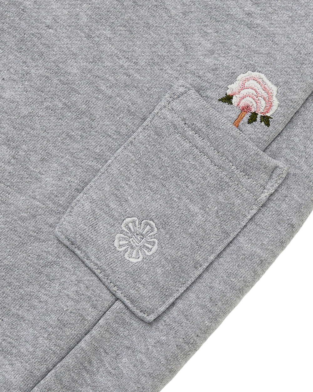 Close-up of the heather gray fabric from Sundae School’s HEATHER GREY WRAP SWEATBAJI, highlighting a small pocket detailed with Korean embroidery—a white flower stitched onto the pocket and a pink flower with a green stem embroidered above it.