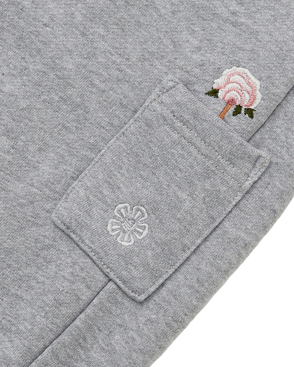 Close-up of the heather gray fabric from Sundae School’s HEATHER GREY WRAP SWEATBAJI, highlighting a small pocket detailed with Korean embroidery—a white flower stitched onto the pocket and a pink flower with a green stem embroidered above it.