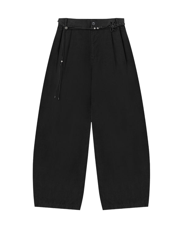 The BLACK FLOWER NORIGAE LINEN TROUSERS by Sundae School are wide-leg, high-waisted black pants with pleats at the top and a thin decorative norigae belt featuring a knotted detail on the right side. These Korean-inspired trousers are laid flat on a white background.