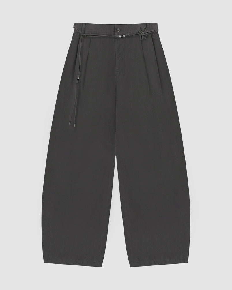 The CHARCOAL FLOWER NORIGAE LINEN TROUSERS by Sundae School are wide-leg black trousers inspired by Korean fashion, featuring a high waist, pleated front, and a thin belt with a knotted detail and small metallic accents, shown flat against a plain light background.