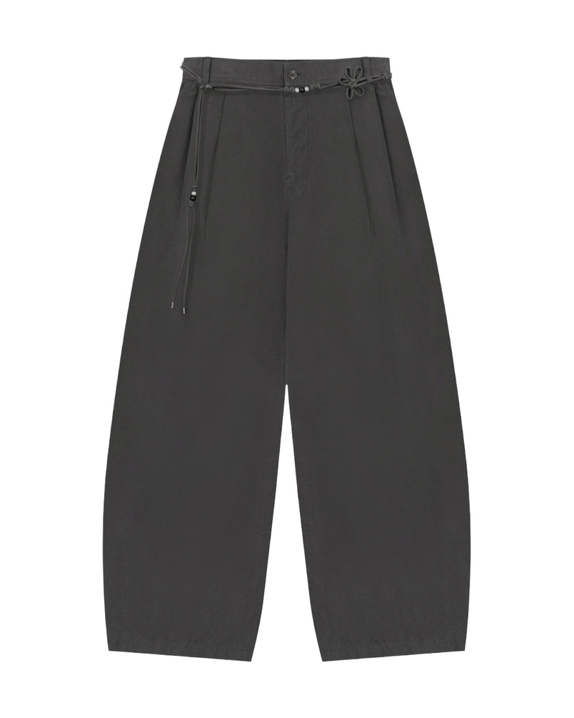 The CHARCOAL FLOWER NORIGAE LINEN TROUSERS by Sundae School are wide-leg black cotton-linen pants featuring pleats, a high waist, and a decorative thin norigae belt with a small knotted accent. Made from soft, slightly textured fabric, these trousers offer a relaxed, modern fit.