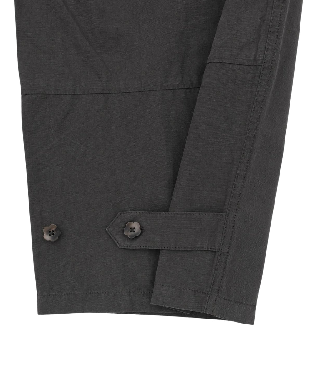 Close-up of a dark gray long sleeve with two black buttons and a stitched strap detail near the cuff, displayed against a white background—perfectly paired with Sundae School’s CHARCOAL FLOWER NORIGAE LINEN TROUSERS for a refined, contemporary look.