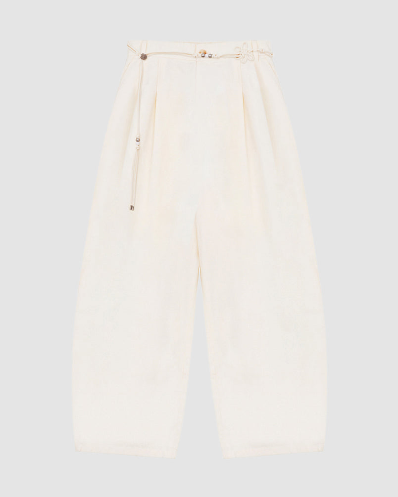 The IVORY FLOWER NORIGAE LINEN TROUSERS by Sundae School, featuring a wide-leg, high-waisted silhouette in cream cotton-linen with front pleats and an attached detachable norigae belt, are laid flat on a light gray background.
