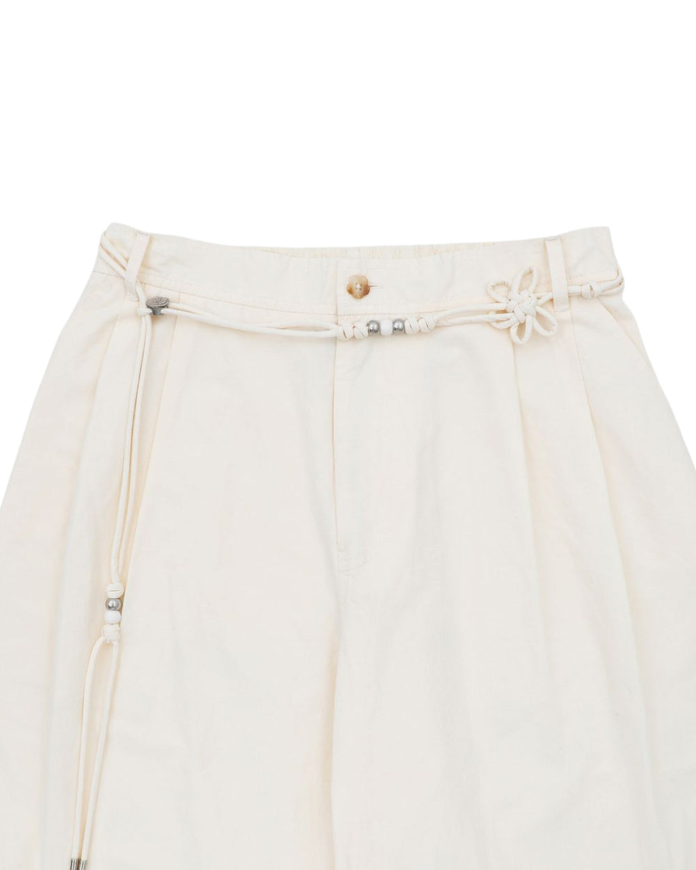 The IVORY FLOWER NORIGAE LINEN TROUSERS by Sundae School are cream-colored, high-waisted cotton linen pants featuring balloon legs and a decorative norigae belt with small metallic beads and a flower-shaped knot detail at the waistband.
