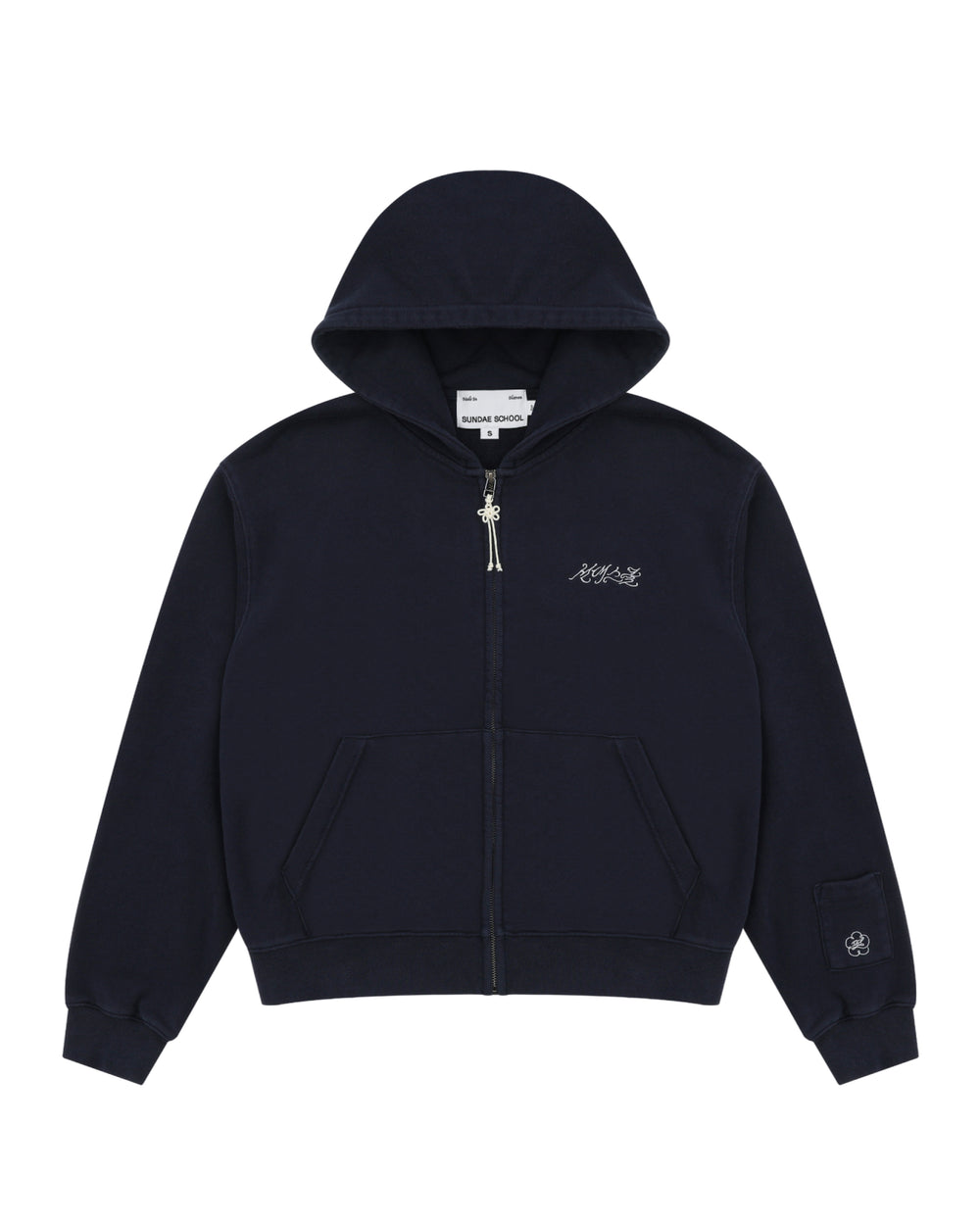 A navy cotton zip-up hoodie by Sundae School featuring front pockets, a small white logo on the left chest, and an embroidered patch with Hangul "Sundae School" on the left sleeve near the cuff. This is the NAVY WASH FLOWER KNOT ZIP UP.