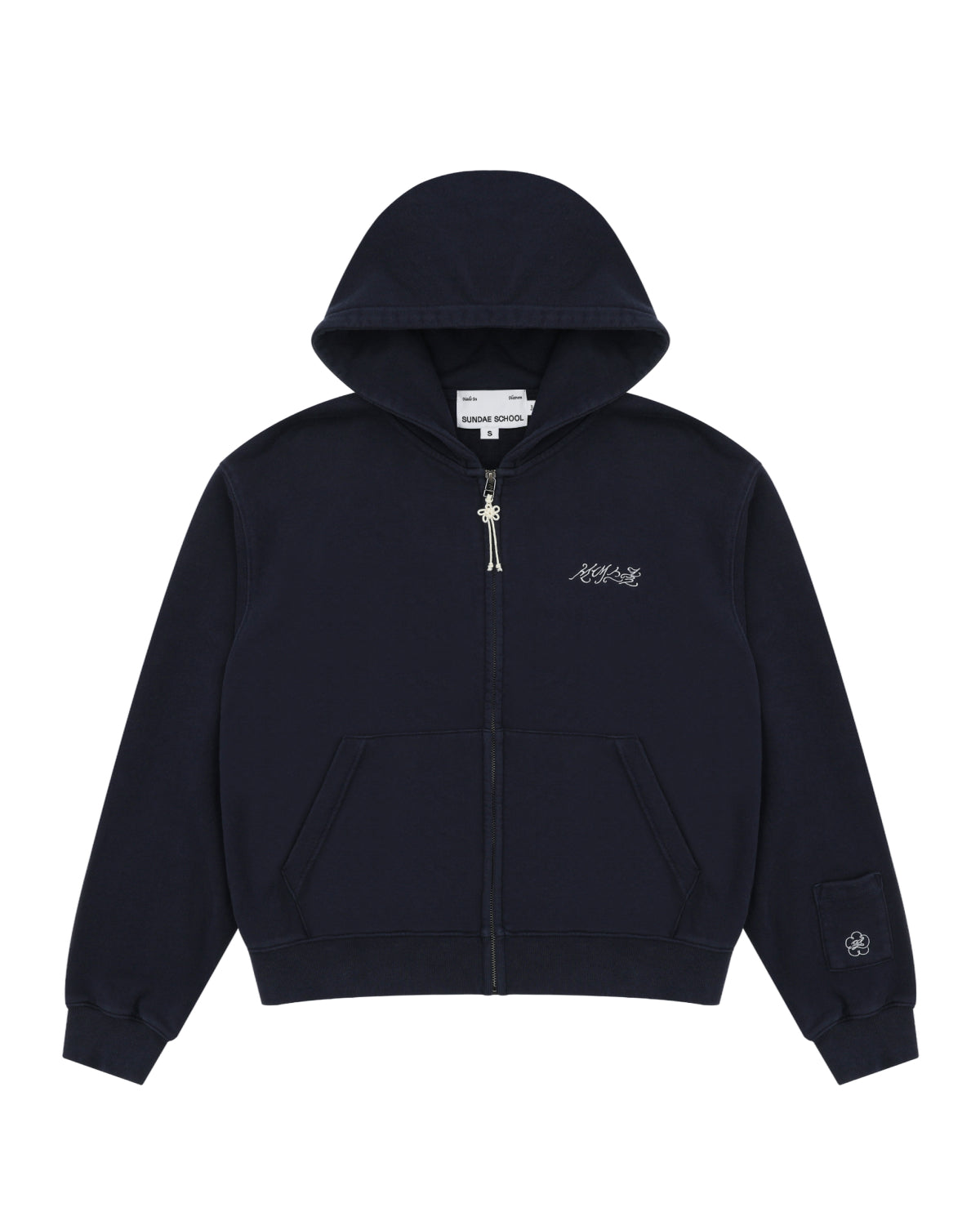 A navy cotton zip-up hoodie by Sundae School featuring front pockets, a small white logo on the left chest, and an embroidered patch with Hangul "Sundae School" on the left sleeve near the cuff. This is the NAVY WASH FLOWER KNOT ZIP UP.