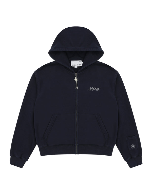 A navy cotton zip-up hoodie by Sundae School featuring front pockets, a small white logo on the left chest, and an embroidered patch with Hangul "Sundae School" on the left sleeve near the cuff. This is the NAVY WASH FLOWER KNOT ZIP UP.