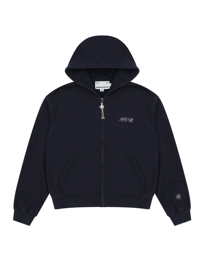 A navy cotton zip-up hoodie by Sundae School featuring front pockets, a small white logo on the left chest, and an embroidered patch with Hangul "Sundae School" on the left sleeve near the cuff. This is the NAVY WASH FLOWER KNOT ZIP UP.