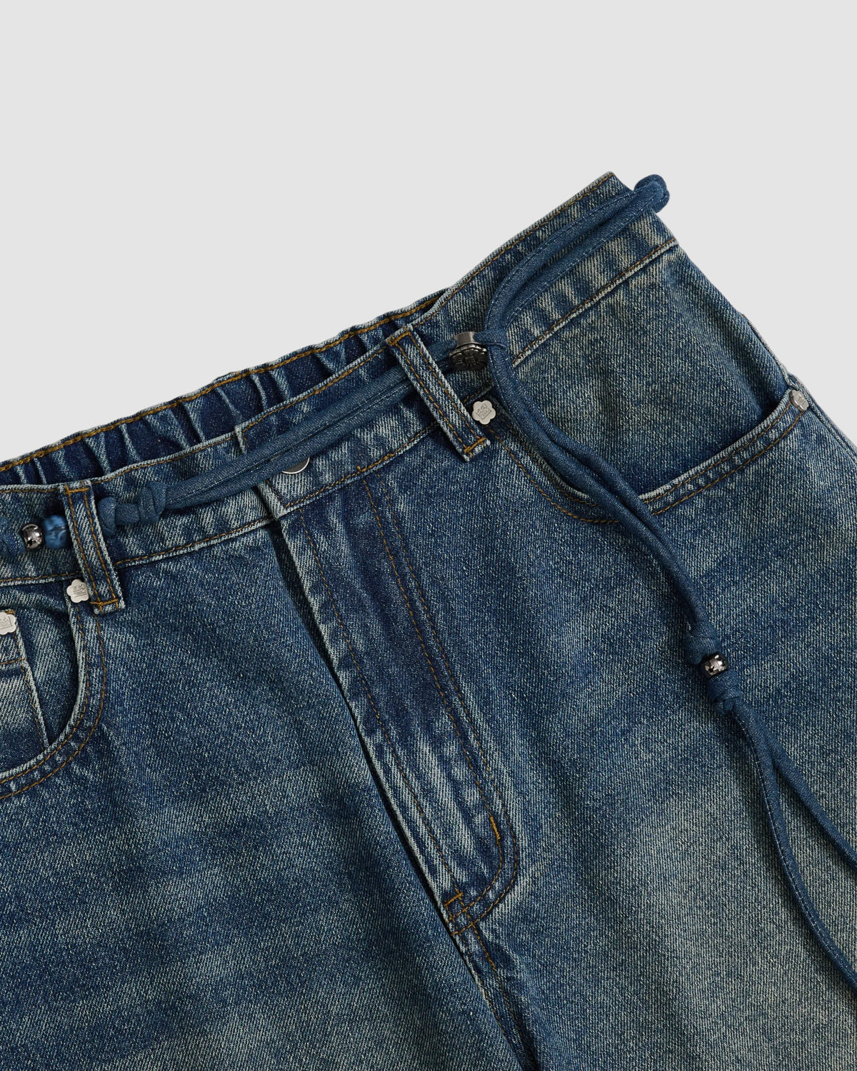 Close-up of Sundae School's MEDIUM BLUE FRESHMAN FIT DENIM: Korean jeans with a drawstring waistband, relaxed straight-leg fit, front pockets, and visible stitching, shown on a light background.