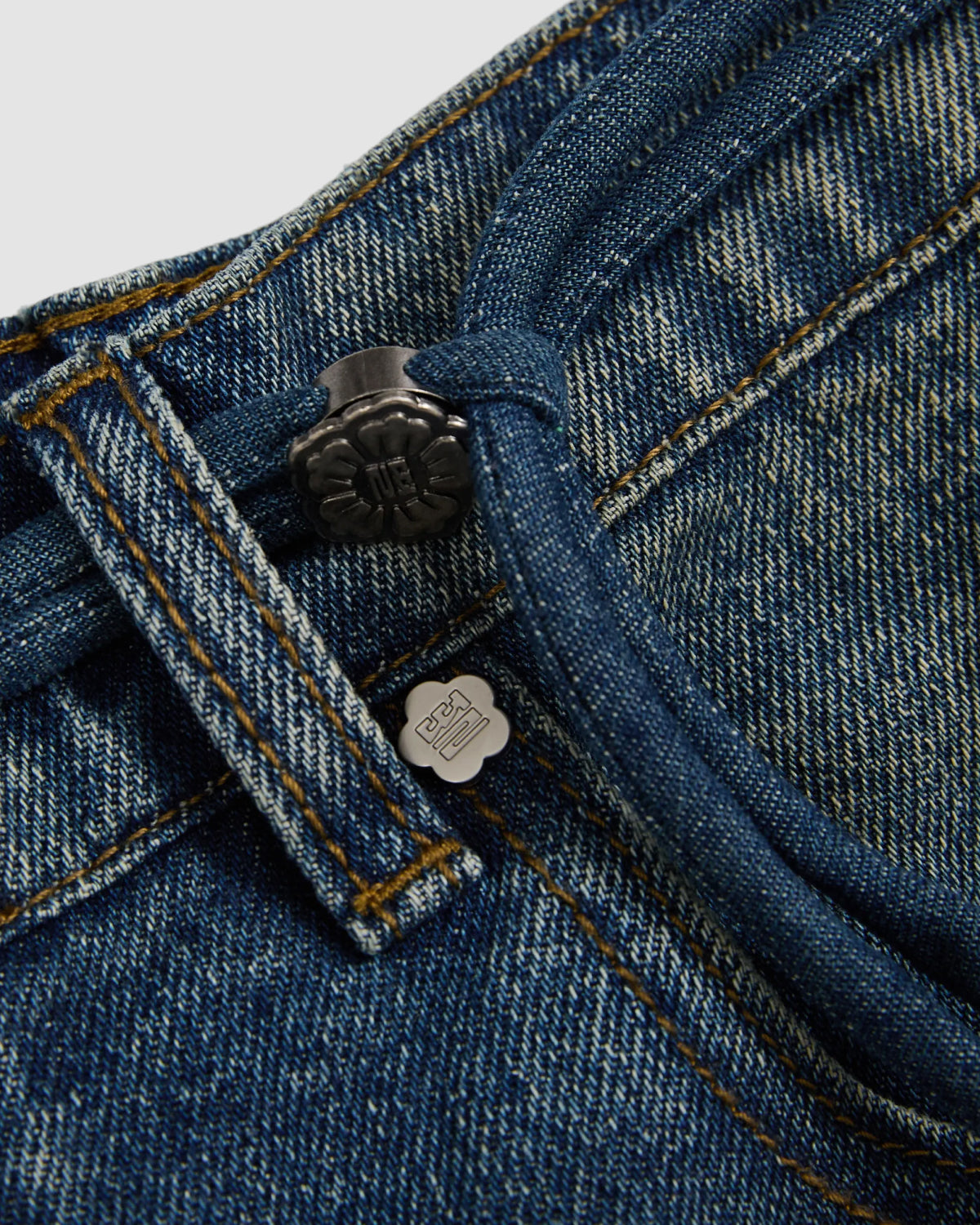Close-up of Sundae School's MEDIUM BLUE FRESHMAN FIT DENIM jeans highlights the button, belt loop, visible stitching, and a small metal tag near the waistband.
