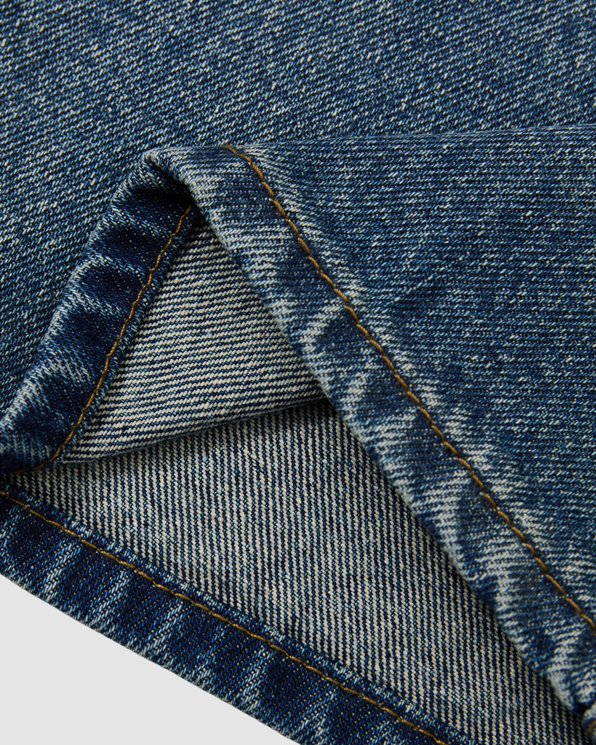 Close-up of Sundae School’s MEDIUM BLUE FRESHMAN FIT DENIM shows the folded edge and visible stitching, highlighting the texture and pattern of this relaxed straight-leg Korean denim fabric.