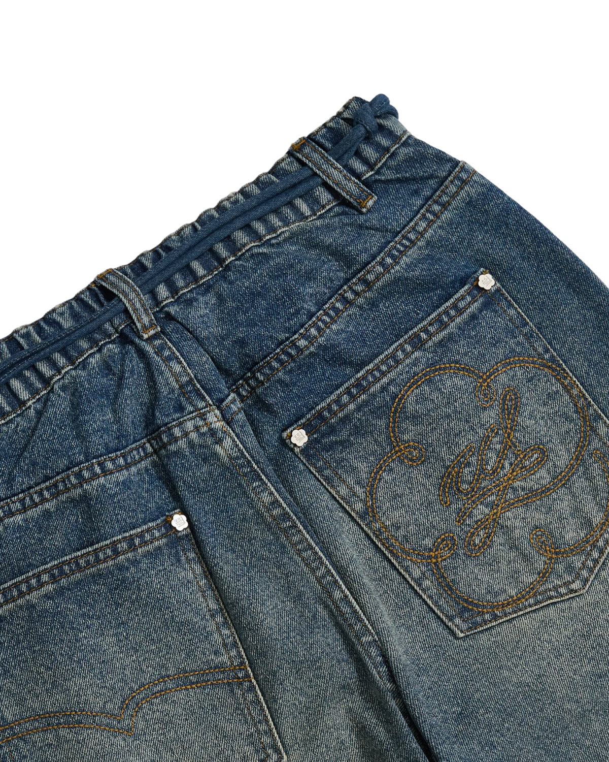 Close-up of Sundae School’s BLUE DREAM FRESHMAN FIT DENIM showcasing the back waist and pockets. One pocket features a decorative, gold embroidered swirl and floral-inspired motif that nods to subtle Korean denim influences. The jeans are finished with metal rivets and an elastic waistband.