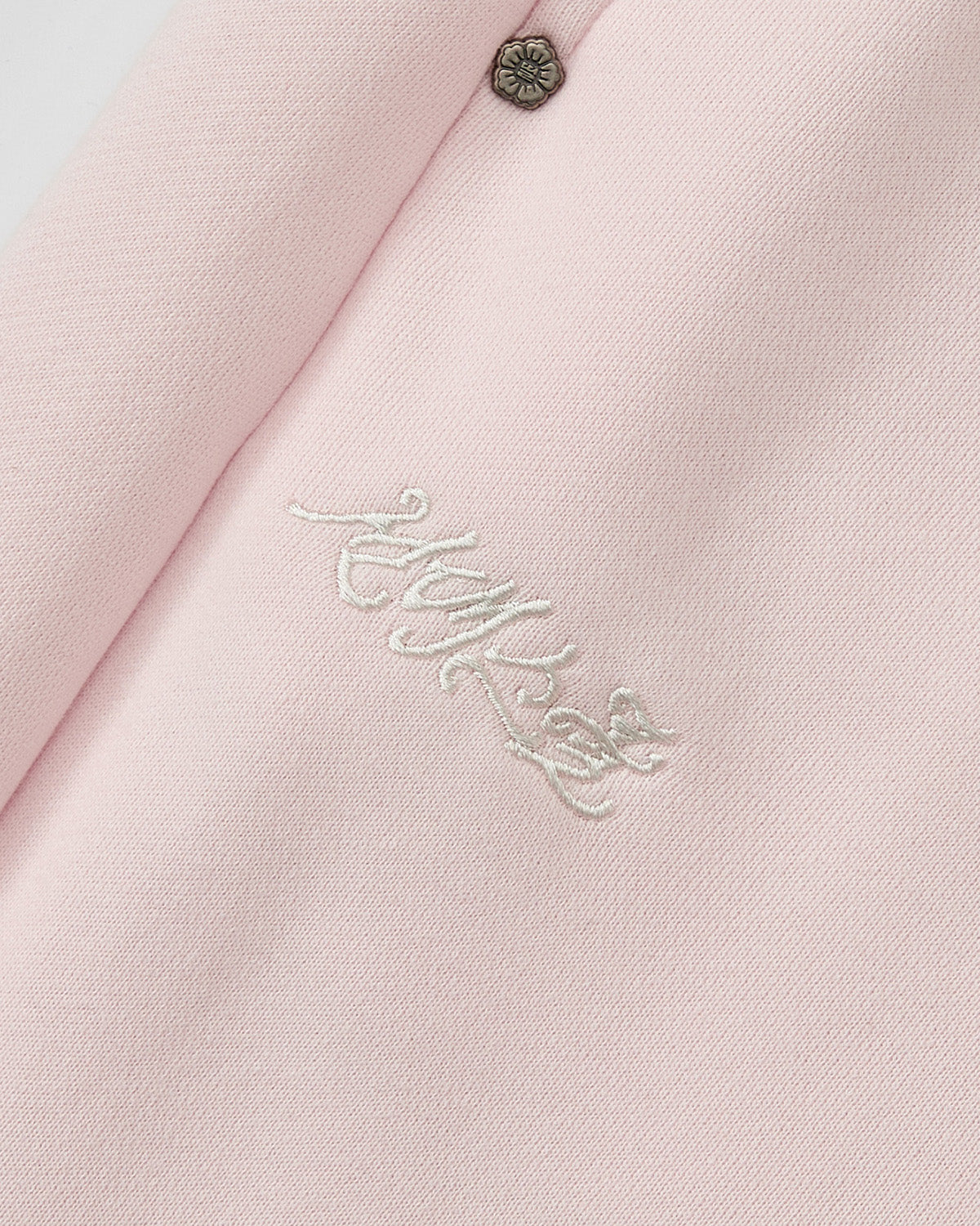 Close-up of BABY PINK WRAP SWEATBAJI by Sundae School: light pink fabric with white Korean embroidery and a small floral metal button at the top, inspired by traditional Hanbok pants.