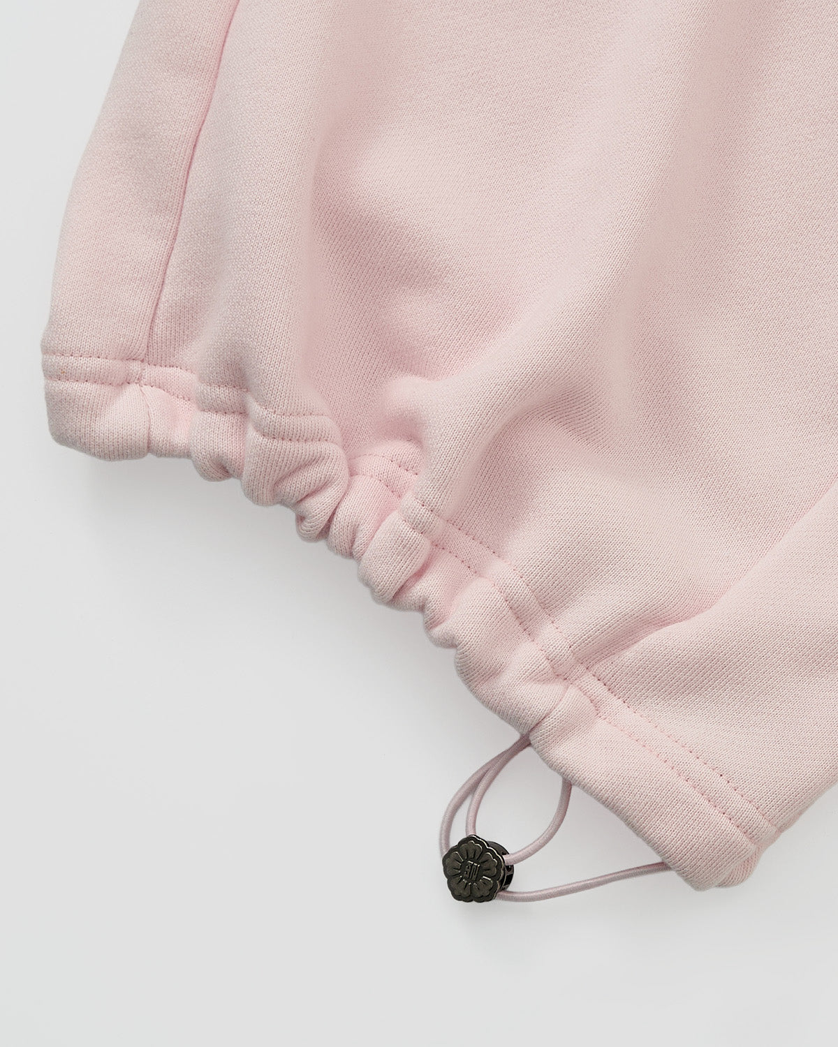 Close-up of the BABY PINK WRAP SWEATBAJI by Sundae School, showing a soft, textured bottom hem with an adjustable drawstring and metallic flower charm, paired with wide leg sweatpants.