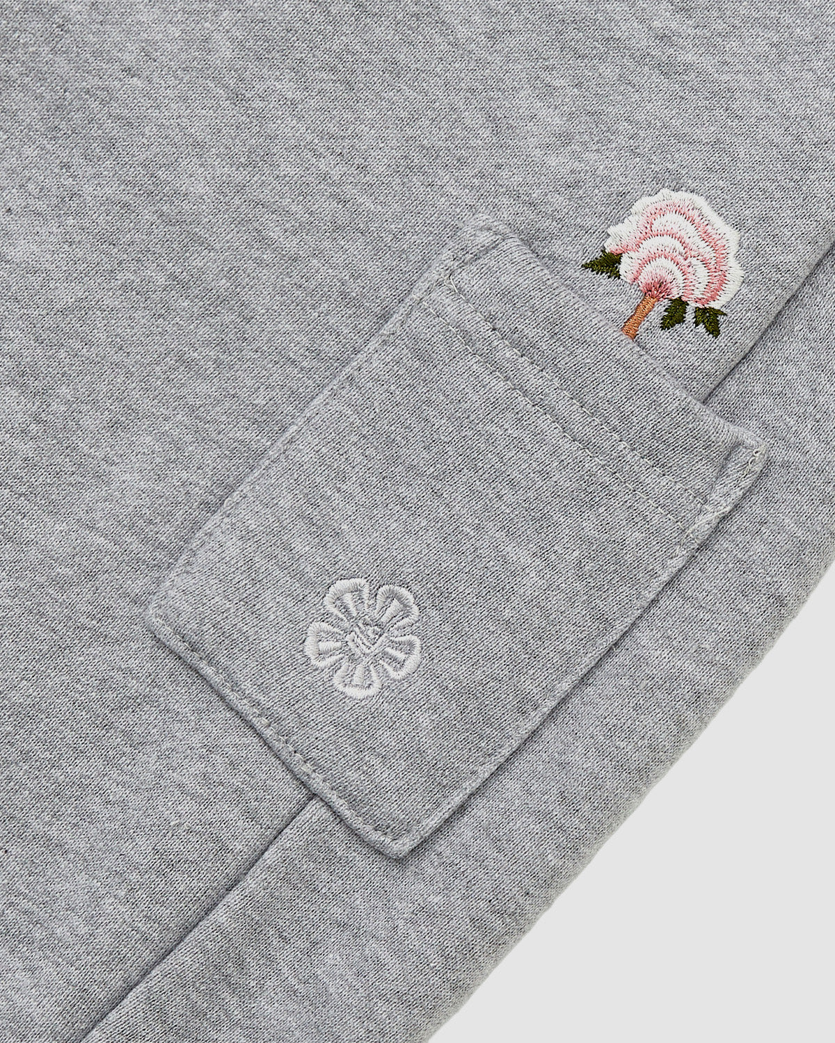 Close-up of Sundae School's HEATHER GREY WRAP SWEATBAJI: gray Hanbok-inspired pants with a small pocket adorned with white flower embroidery, topped by an embroidered pink flower with a green stem and brown outline.