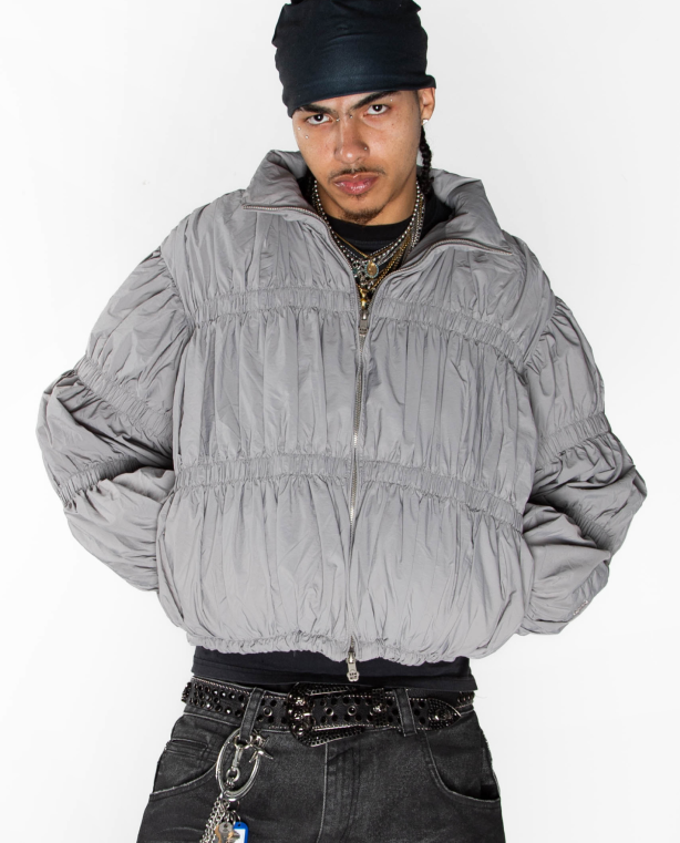 The Sundae School SMOKE PLEATED DUVET PUFFER is a light gray zip-up jacket with a high collar, all-over pleated ruching for texture and volume, long sleeves, and an elastic hem.