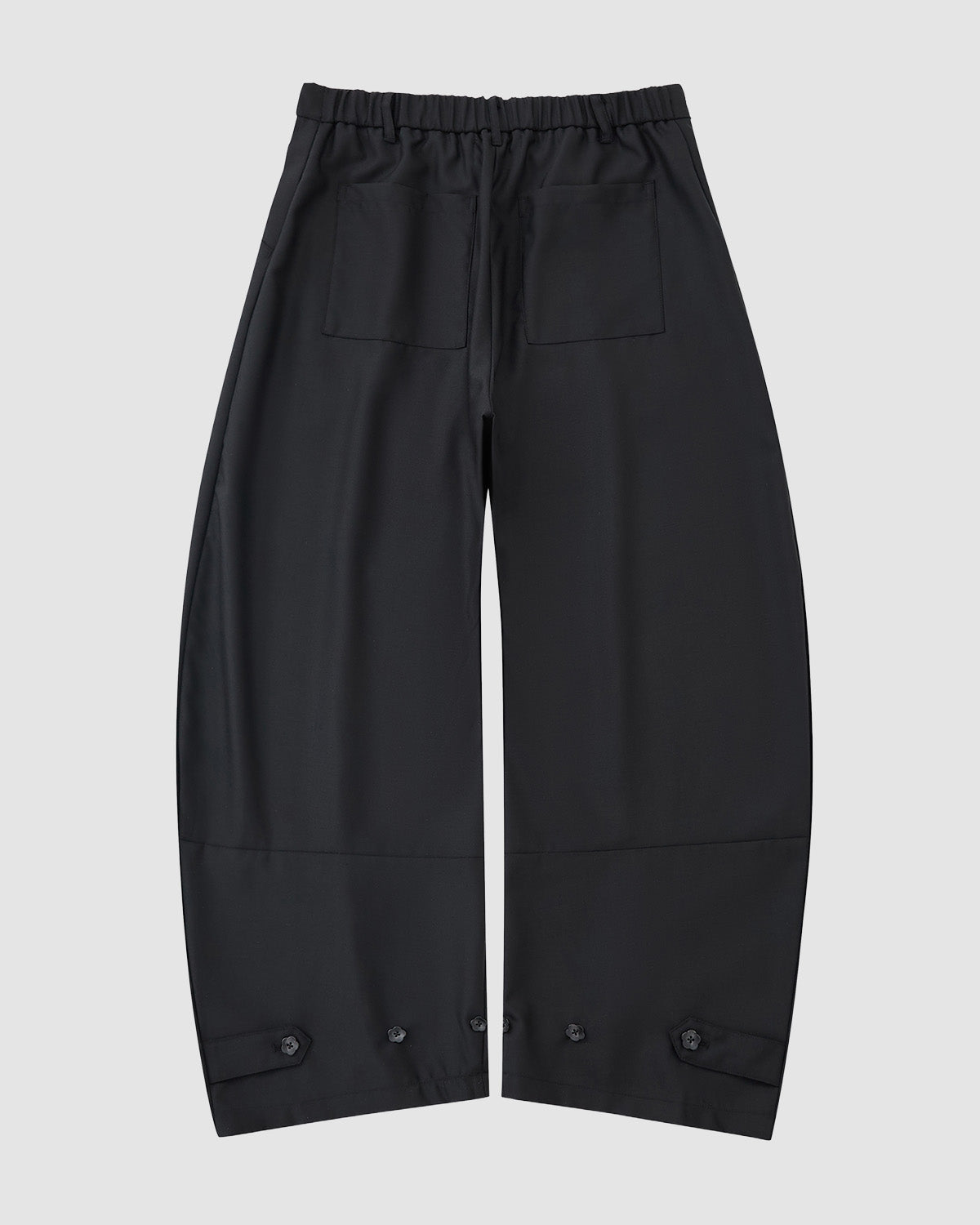 The BLACK PLEATED HANBOK SLACKS by Sundae School are loose-fitting black pants with an elastic waistband, two front patch pockets, and button details at the hems, shown on a light gray background.