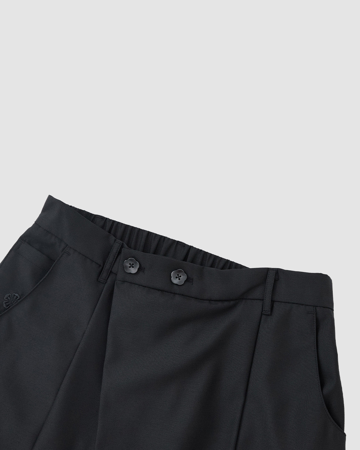 The BLACK PLEATED HANBOK SLACKS by Sundae School, unisex wool pants with a tailored waistband, button closure, belt loops, and side pockets, are shown laid flat on a light grey background for timeless style and comfort.