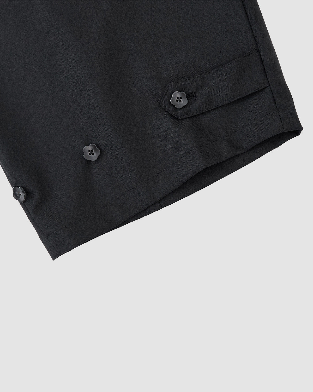 Close-up of the hem of Sundae School’s BLACK PLEATED HANBOK SLACKS, showing three black buttons and a small flap with a buttoned tab against a plain light gray background.