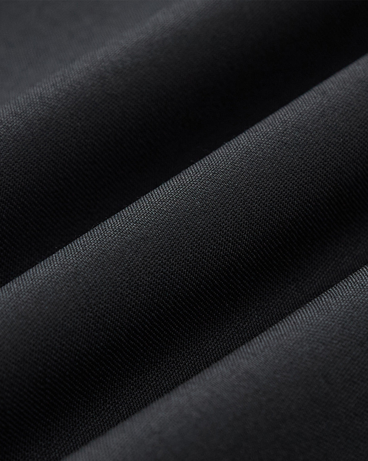 Close-up of Sundae School's BLACK PLEATED HANBOK SLACKS shows fine, smooth black fabric with soft folds, creating gentle shadows and highlights—ideal for unisex wear and perfect for modern Hanbok balloon pants.
