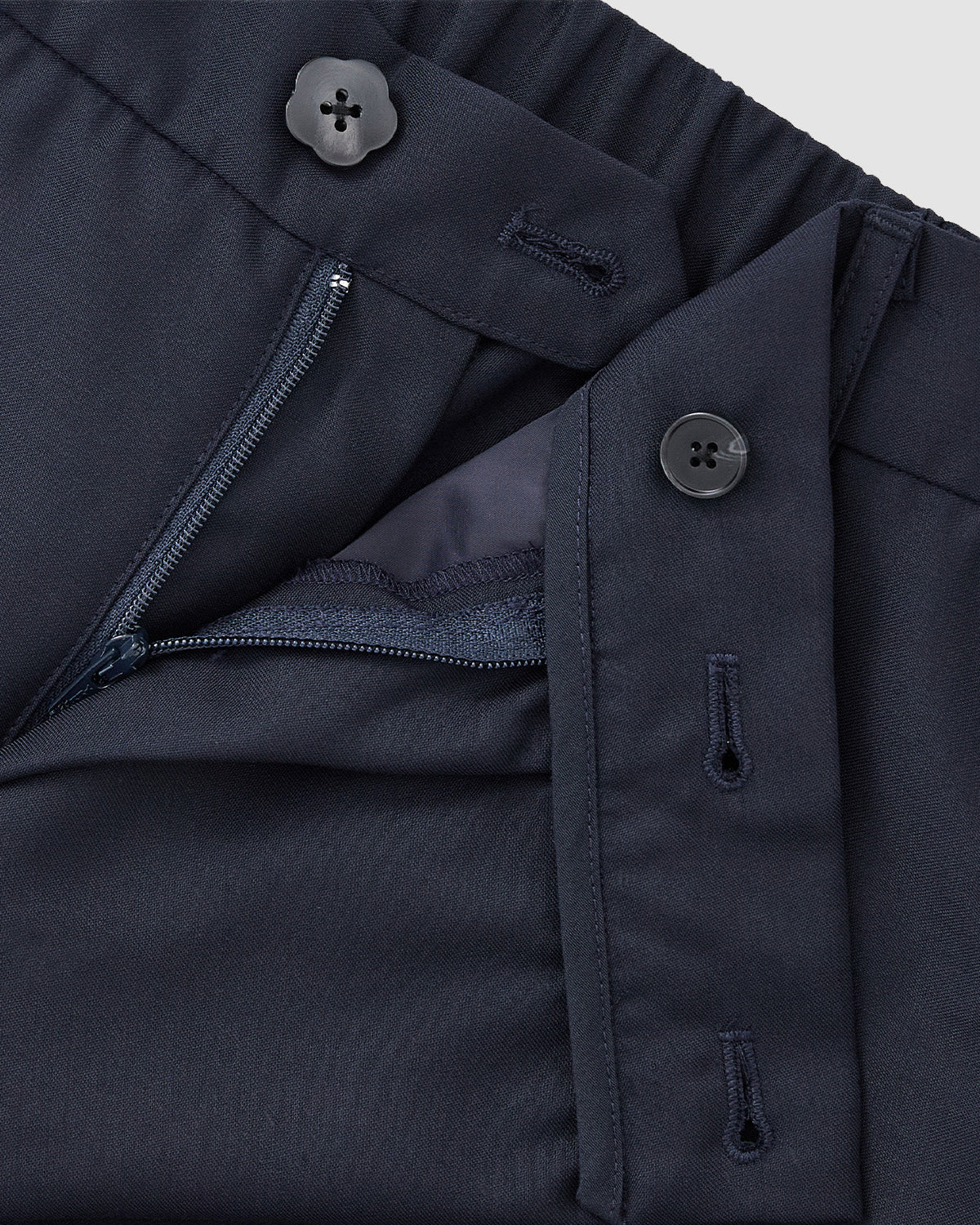 Close-up of Sundae School's NAVY PLEATED HANBOK SLACKS in navy blue wool blend. These unisex pants feature a partially open zipper, visible inner lining, button closure at the waistband, and an extra button on the tab above the zipper.