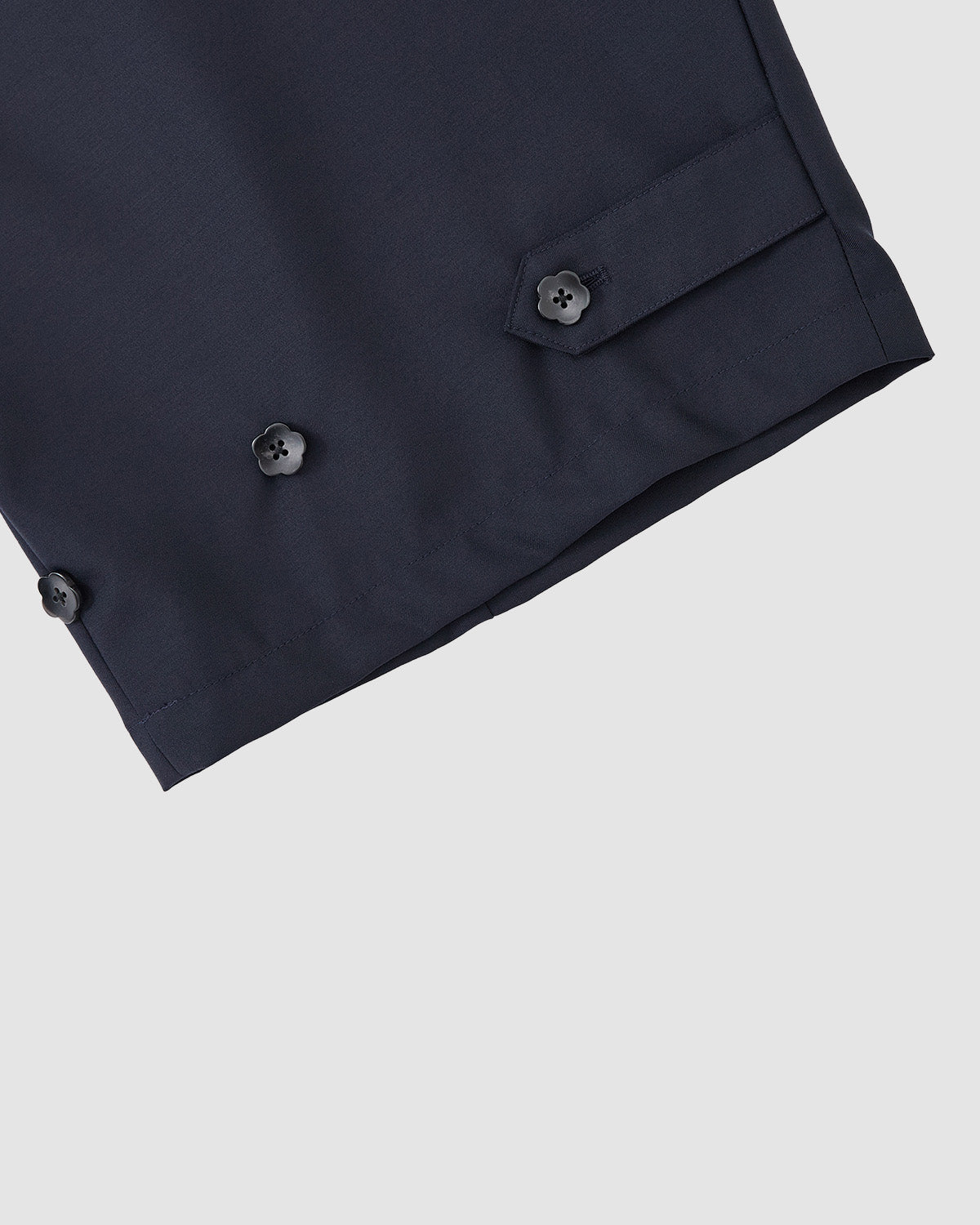 Close-up of the hem of Sundae School’s NAVY PLEATED HANBOK SLACKS, featuring three black buttons and a buttoned tab detail on navy blue wool blend, set against a light gray background.