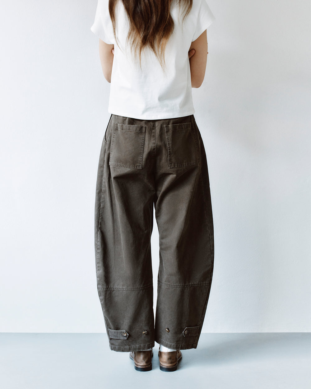 Back view of a person wearing olive green, high-waisted, wide-leg SOIL HANBOK CHINO PANTS with back patch pockets and adjustable button tabs at the cuffs.