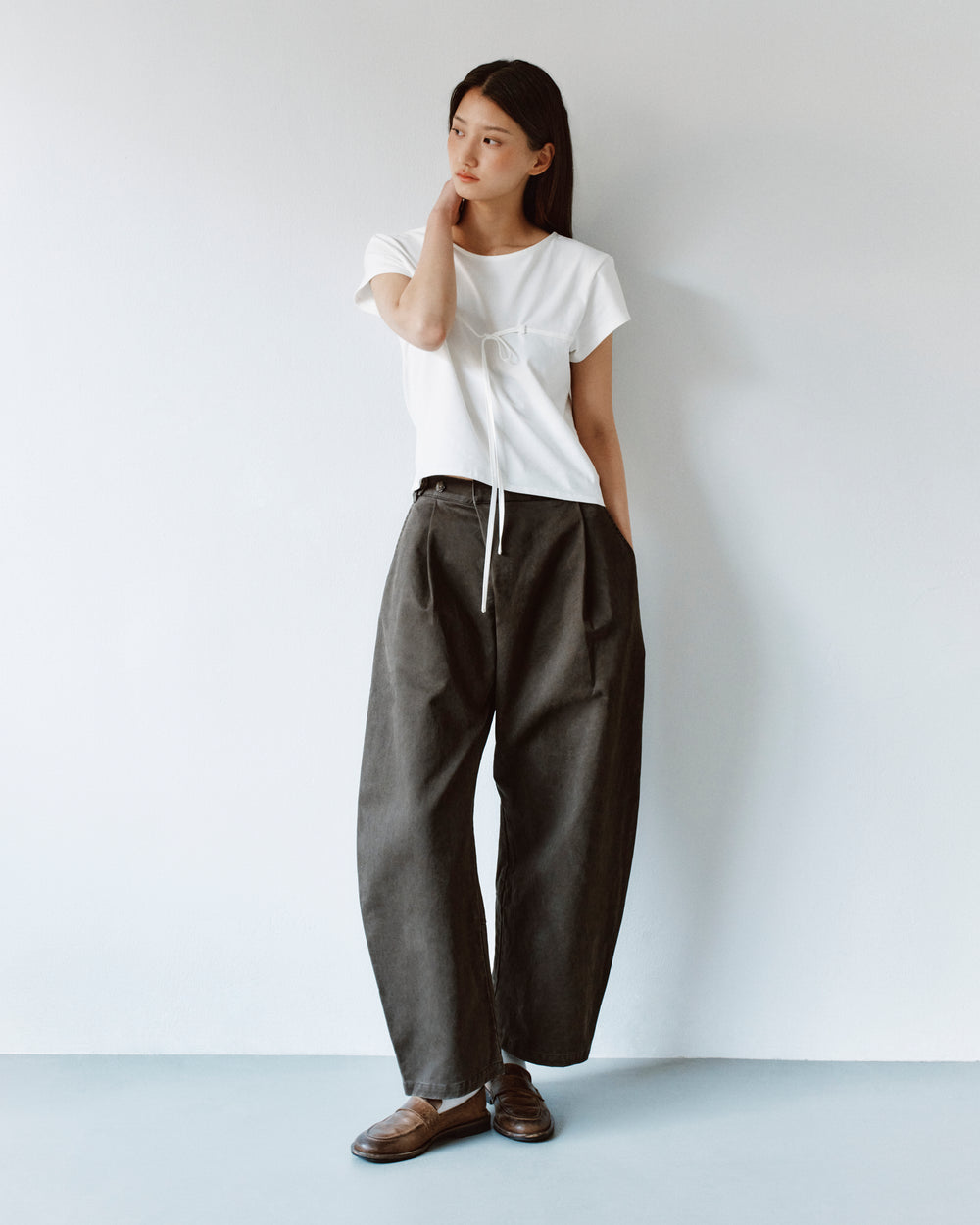 A person wears a white front-tie t-shirt and charcoal-grey SOIL HANBOK CHINO PANTS, paired with brown loafers.