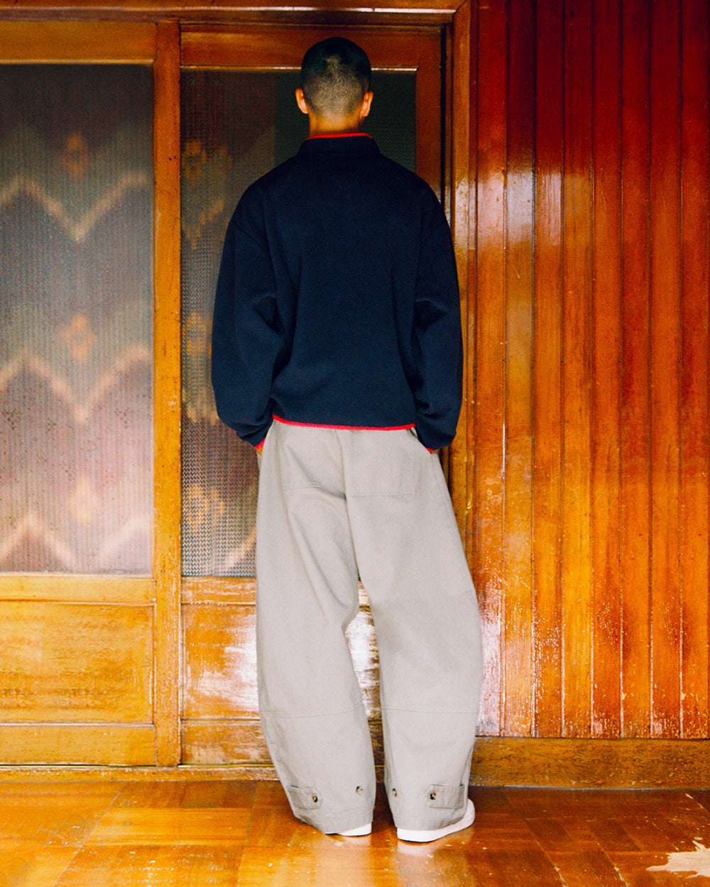 A person seen from behind wearing grey STONE KIEF HANBOK CHINO PANTS with buttoned cuffs and a dark long-sleeved shirt with red trim.