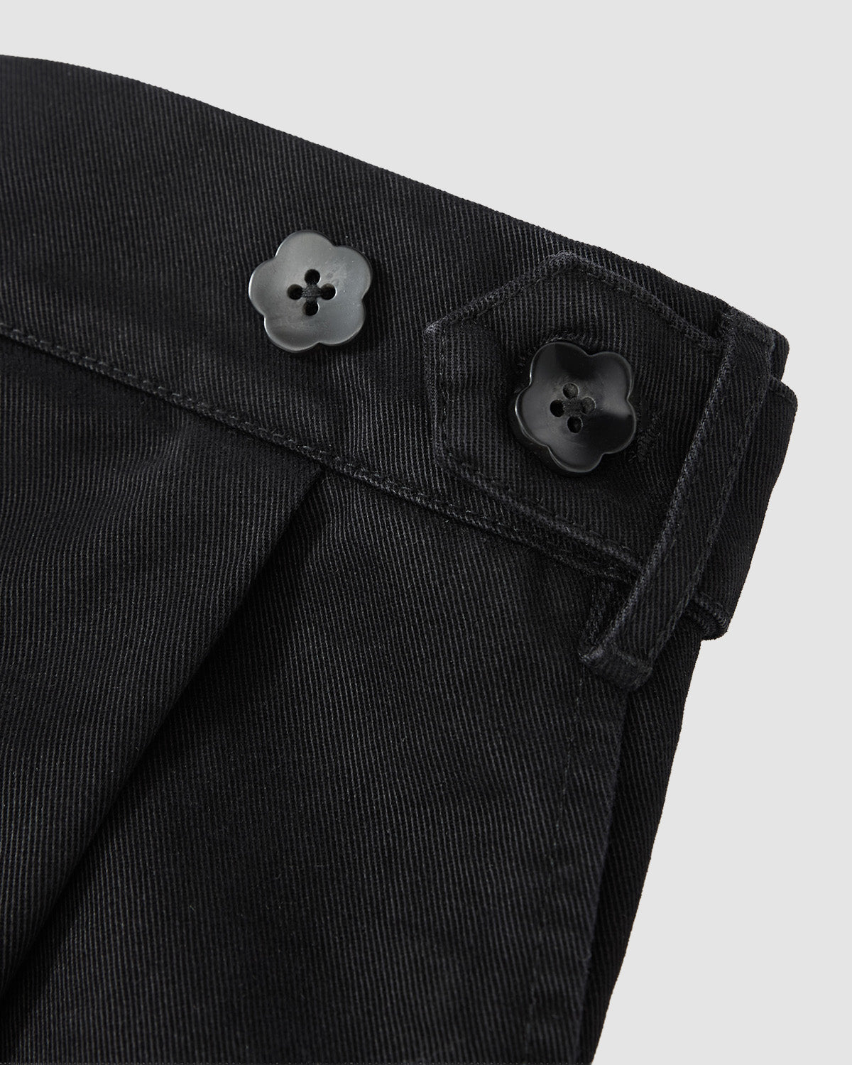 Close-up of Sundae School BLACK HANBOK CHINO PANTS featuring two black flower-shaped buttons, a belt loop, detailed stitching on dark fabric, and a hanbok-inspired silhouette.
