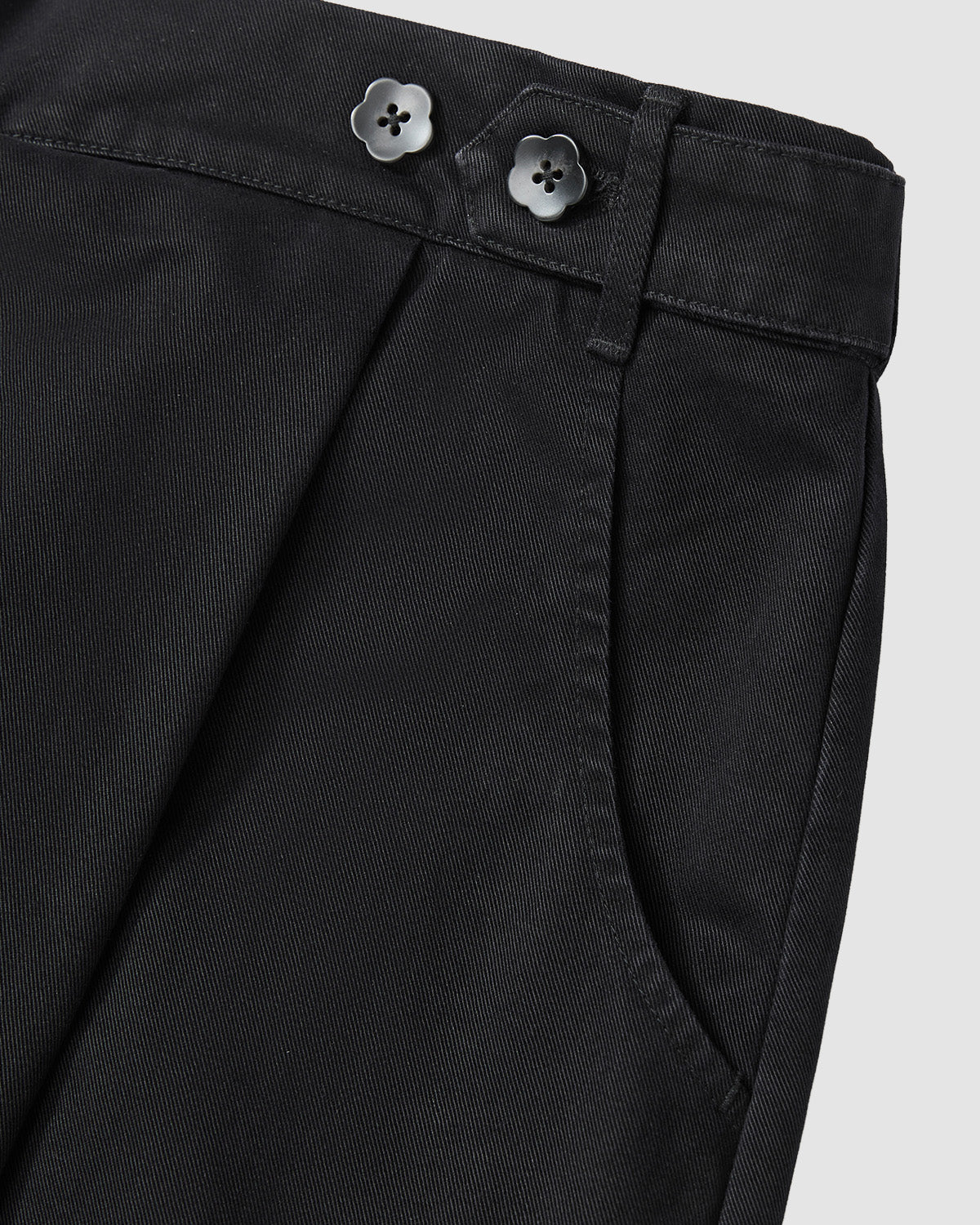 Close-up of Sundae School BLACK HANBOK CHINO PANTS featuring a hanbok-inspired silhouette, side pocket, pleated details, and two black flower-shaped buttons on the waistband, shown against a light grey background.