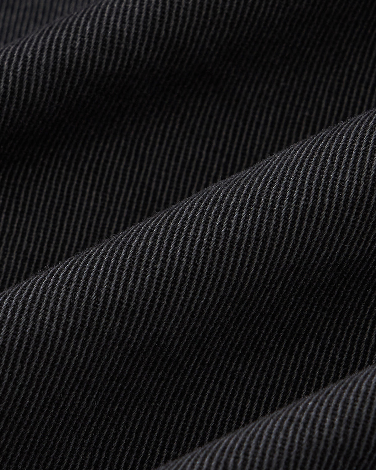 Close-up of Sundae School BLACK HANBOK CHINO PANTS shows black ribbed fabric with diagonal lines and soft folds, highlighting the fine weave and unique texture.