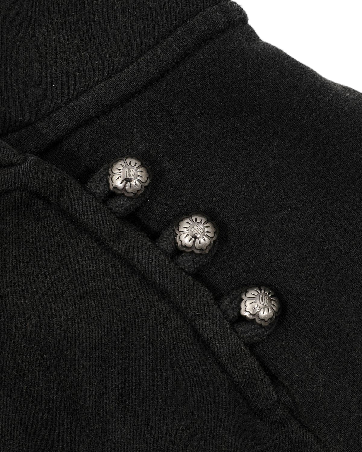 Close-up of the BLACK WASH HANBOK HOODIE by Sundae School, crafted from black cotton fabric and featuring three metallic flower-shaped buttons arranged diagonally, each button adorned with a small engraved design at the center.