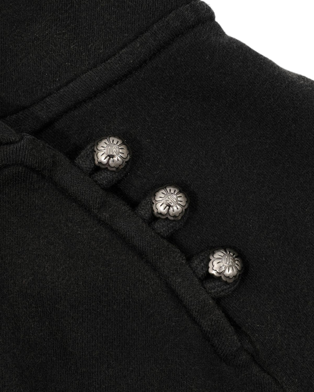 Close-up of the BLACK WASH HANBOK HOODIE by Sundae School, crafted from black cotton fabric and featuring three metallic flower-shaped buttons arranged diagonally, each button adorned with a small engraved design at the center.