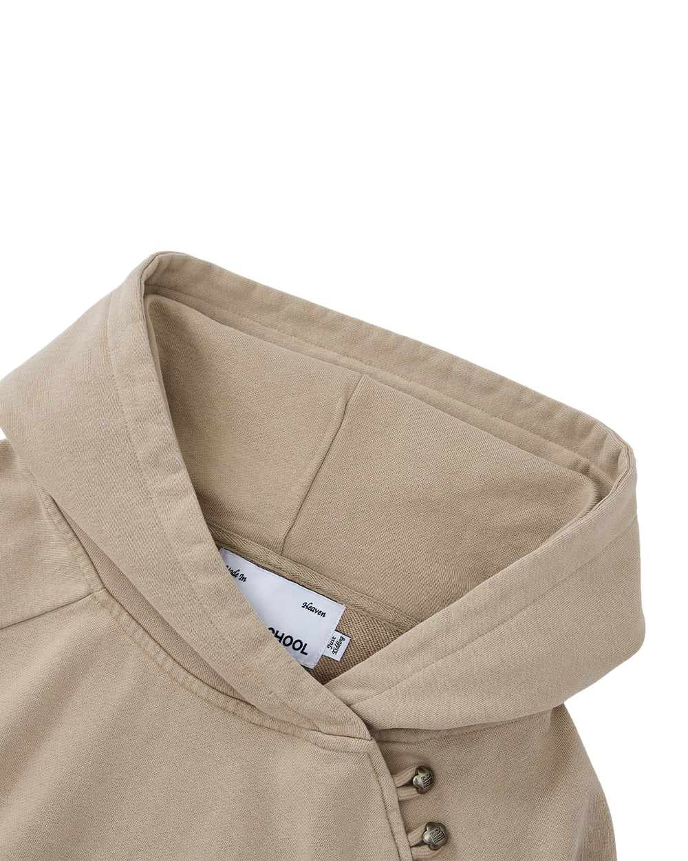A close-up of Sundae School’s TAUPE HANBOK HOODIE showcases its beige color, distinctive wide collar, and asymmetric hood closure with metal snap buttons on one side, as well as a visible white tag inside the neckline. The signature stash pocket enhances both the style and functionality of this unique piece.