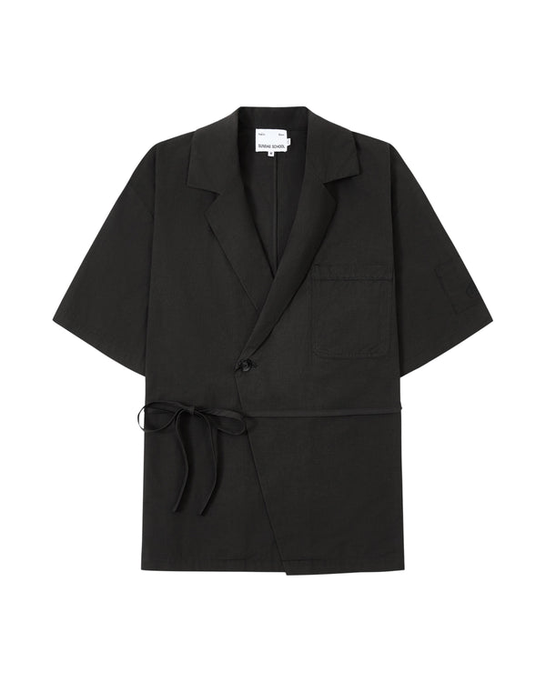 The BLACK HANBOK LINEN SHIRT by Sundae School is a black, short-sleeve blazer-style jacket inspired by the cotton linen hanbok, featuring a chest pocket, side tie closure, single button, and notched lapels, laid flat on a white background.