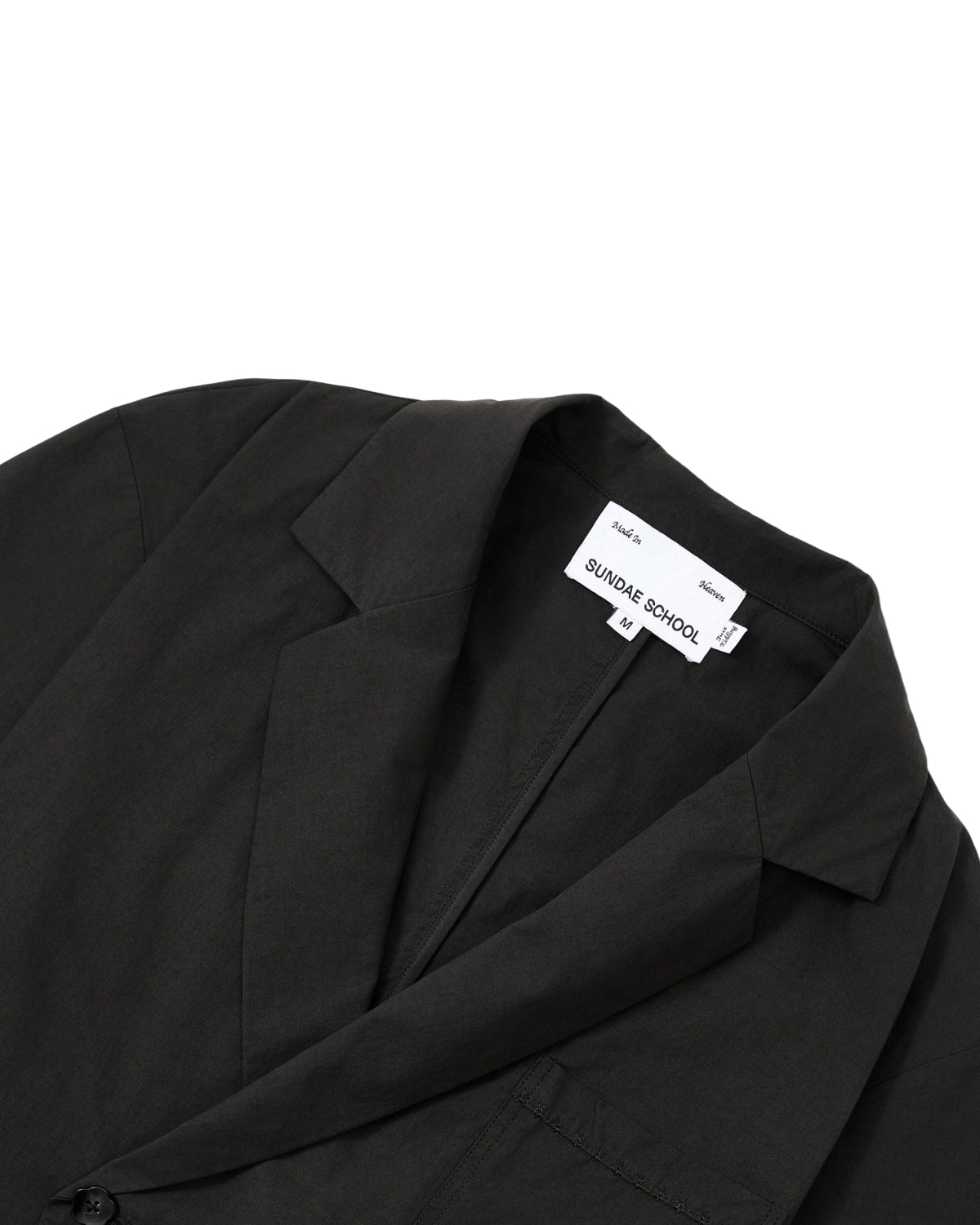 Close-up of the BLACK HANBOK LINEN SHIRT by Sundae School. Drawing inspiration from the refined minimalism of a summer hanbok, it features smooth, slightly matte fabric reminiscent of modern cotton linen hanbok materials. The inner label displays “Sundae School” with size L printed below.