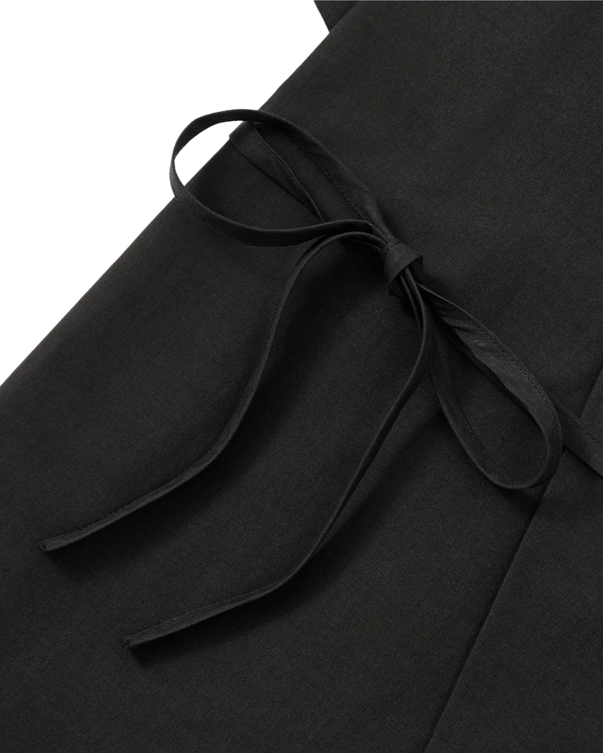 Close-up of the BLACK HANBOK LINEN SHIRT by Sundae School, showcasing a tied bow crafted from matching fabric straps, displayed flat against the black linen cotton material.